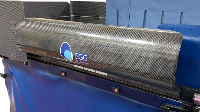 ScatterScoop in place along the side of an EggNest table, its carbon fiber shell above the blue table skirt