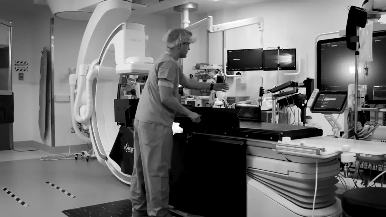 A clinician in scrubs at the EggNest table in a cath lab, in black and white